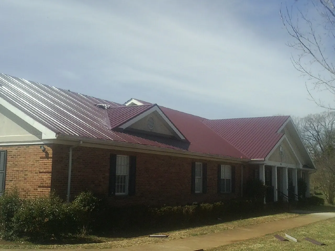 Red metal roof with gabled entries on a long brick building, from a Hail Damage Roof Repair job in Lorton